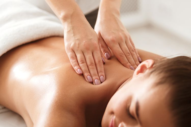 Close‑up of a therapist pressing both hands into a woman’s oiled back during a relaxation massage.