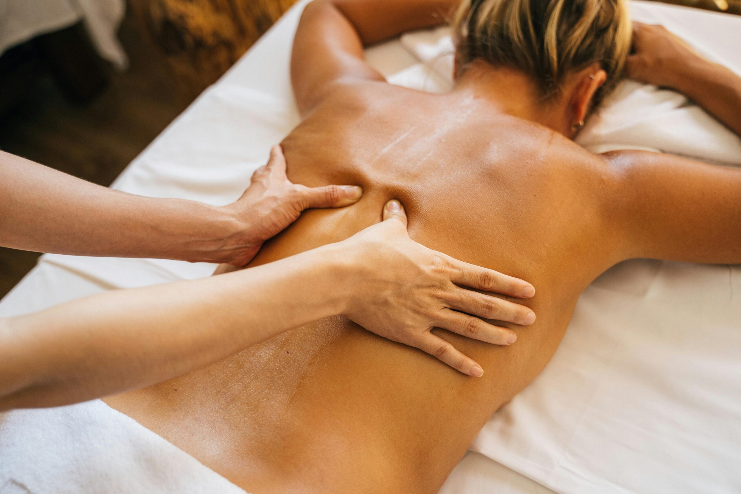 Therapist performs a deep tissue stroke along a woman’s oiled back.