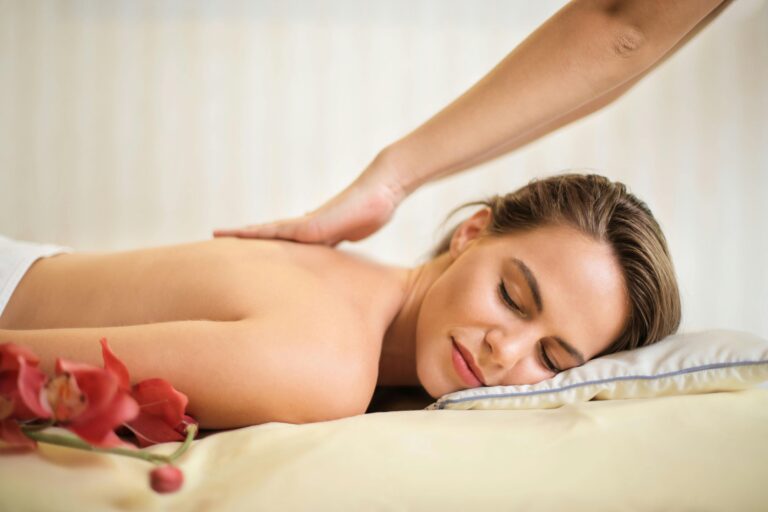 Smiling woman lies face‑down receiving a soothing back massage beside red orchids.
