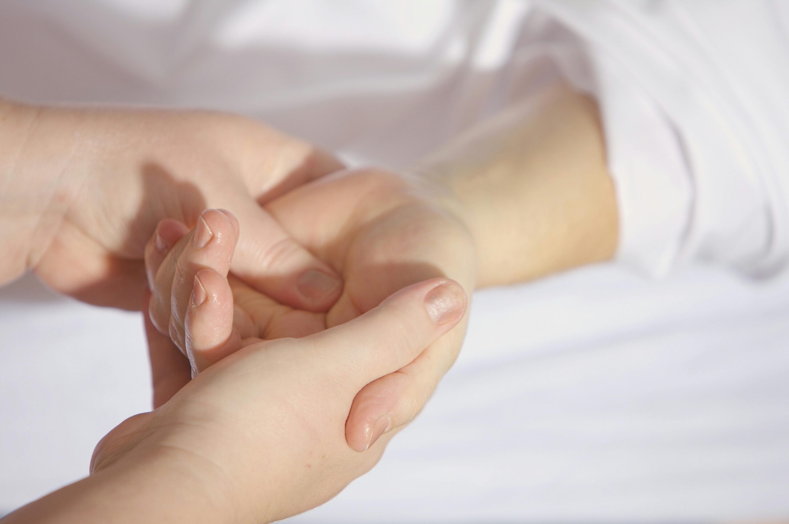 Close‑up of therapist gently massaging a client’s palm over white linens.