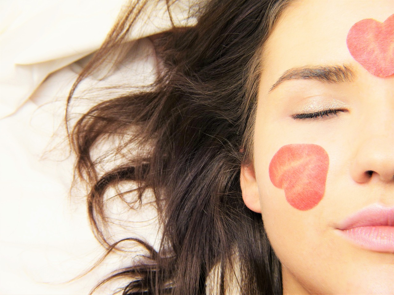 Close‑up of woman’s face with heart‑shaped petals on her cheeks, eyes peacefully closed.