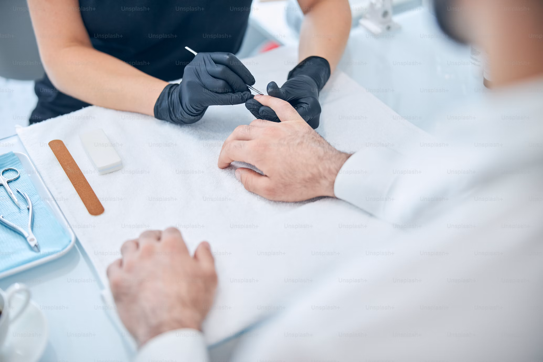 Man receiving a manicure as a gloved technician works on his fingernails over a white towel.